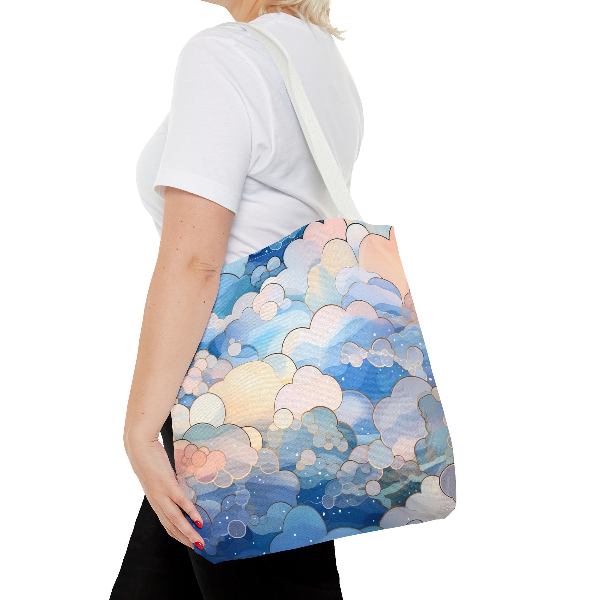 A person holds a Stained Glass Clouds Tote Bag, Blue, featuring a vibrant cloud pattern in blue, pink, and white. Theyre wearing a white t-shirt and black pants against a white backdrop.