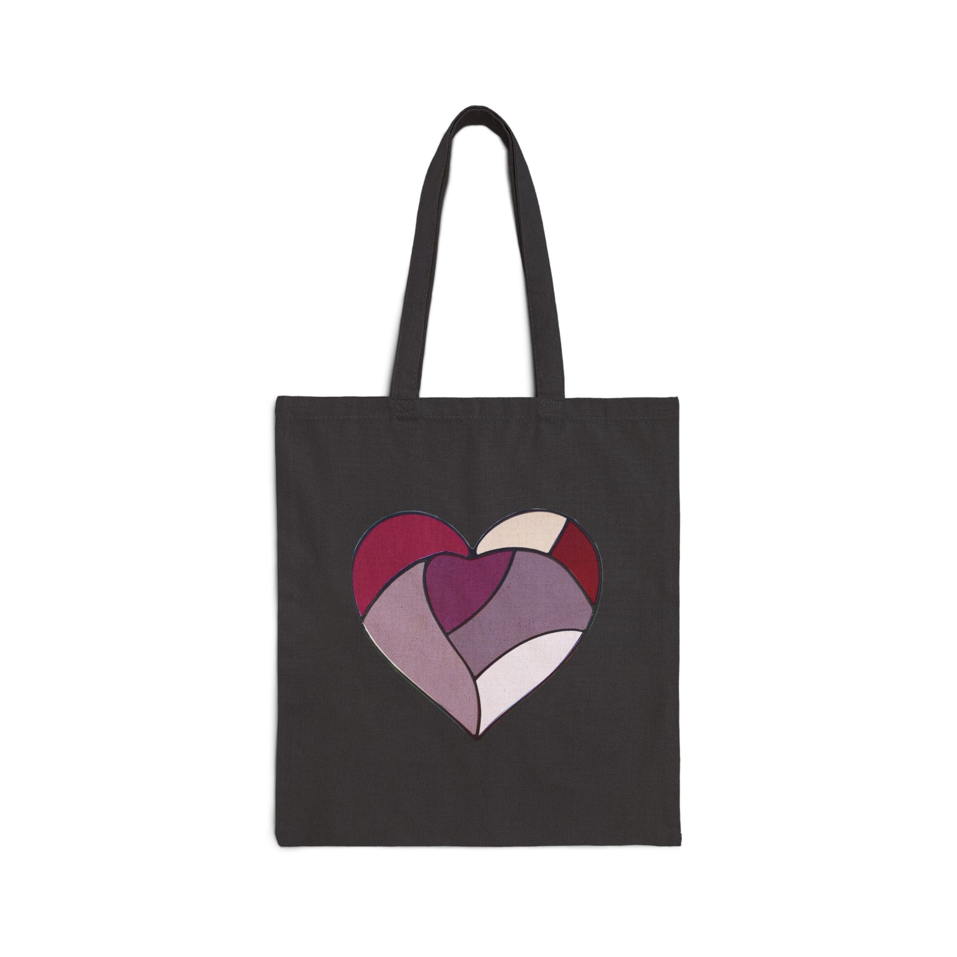 A person with curly hair wearing a white t-shirt and jeans is holding the Stained Glass Heart Cotton Canvas Tote Bag featuring a floral stained glass design in a circular pattern over their shoulder.