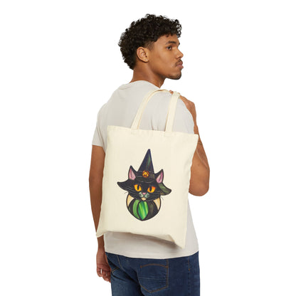 Wearing jeans and a light gray t-shirt, a person carries the beige Stained Glass Cat Witch Cotton Canvas Tote Bag on their shoulder. The bag features a vibrant stained glass design of a black cat wearing an orange-adorned witch hat against a plain white backdrop.