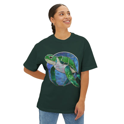 A person wearing an oversized stained glass turtle tee shirt, featuring a colorful sea turtle design by Noelle Barnes, is smiling and looking to the side.