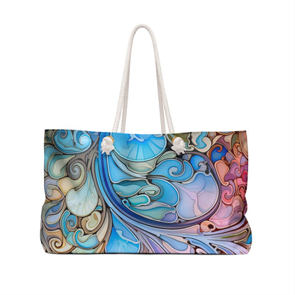 The Rainbow Paisley Stained Glass Oversized Tote Bag features a bohemian-style abstract pattern with swirling shapes in blue, pink, and brown. It includes white rope handles attached by knots, making it perfect for adding a splash of color to any outfit.