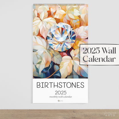 The birthstomes calendar, a 2025 monthly wall calendar with gem-themed original artwork, on a wood table surface. 