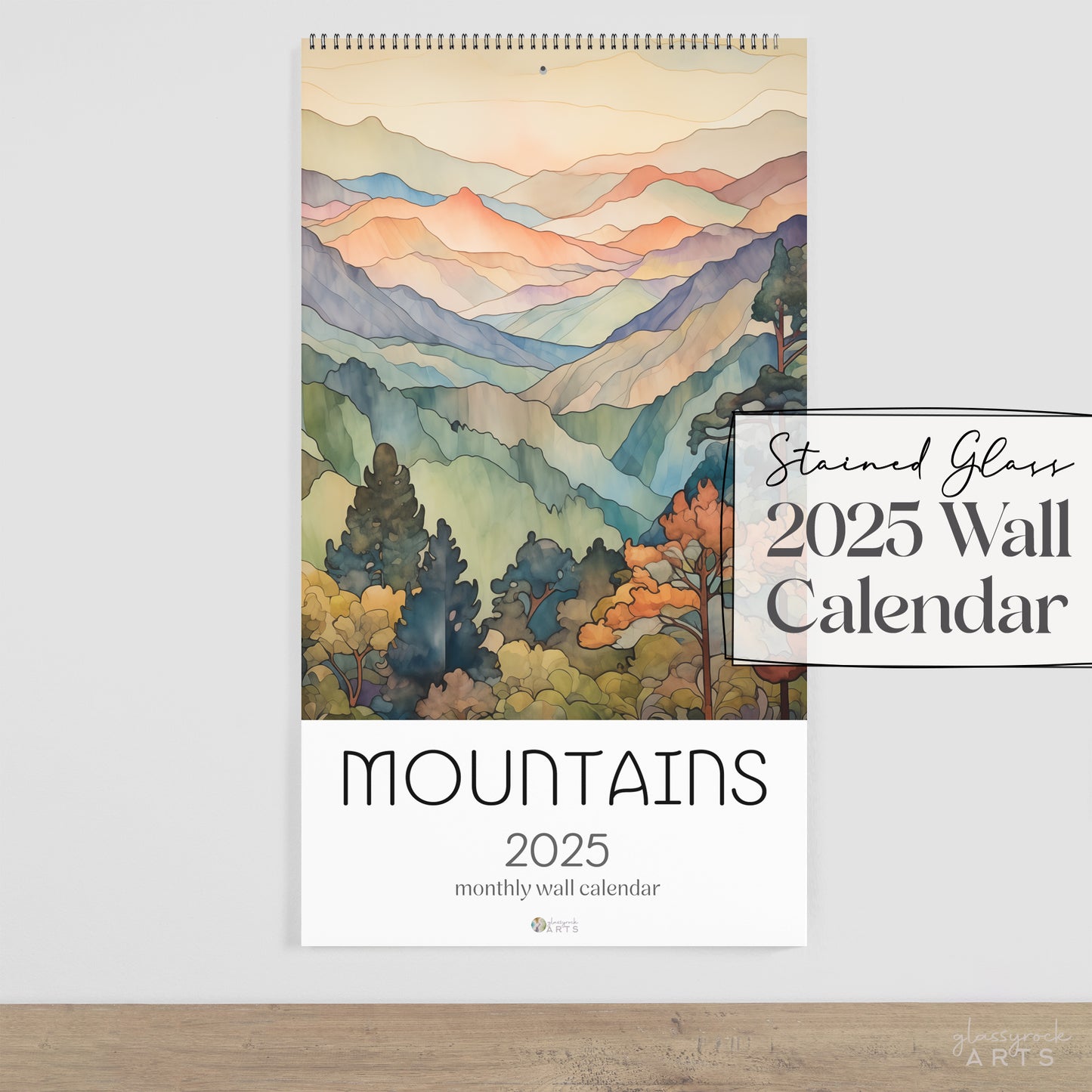 The 2025 stained glass mountains wall calendar on a white wall. 