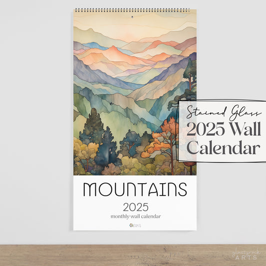 The 2025 stained glass mountains wall calendar on a white wall. 