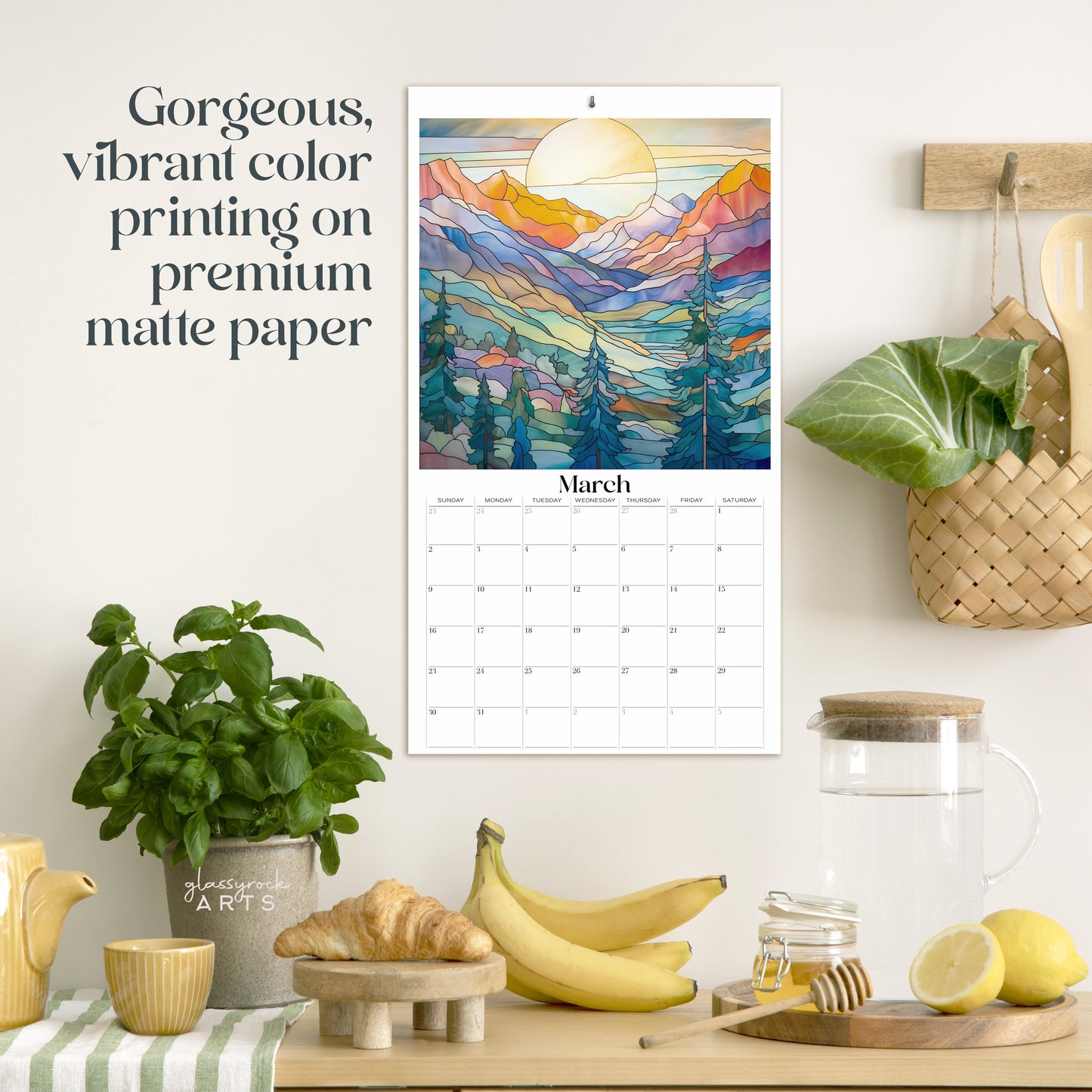 The 2025 stained glass mountains wall calendar on a kitchen wall with plants. The March page is showing. 