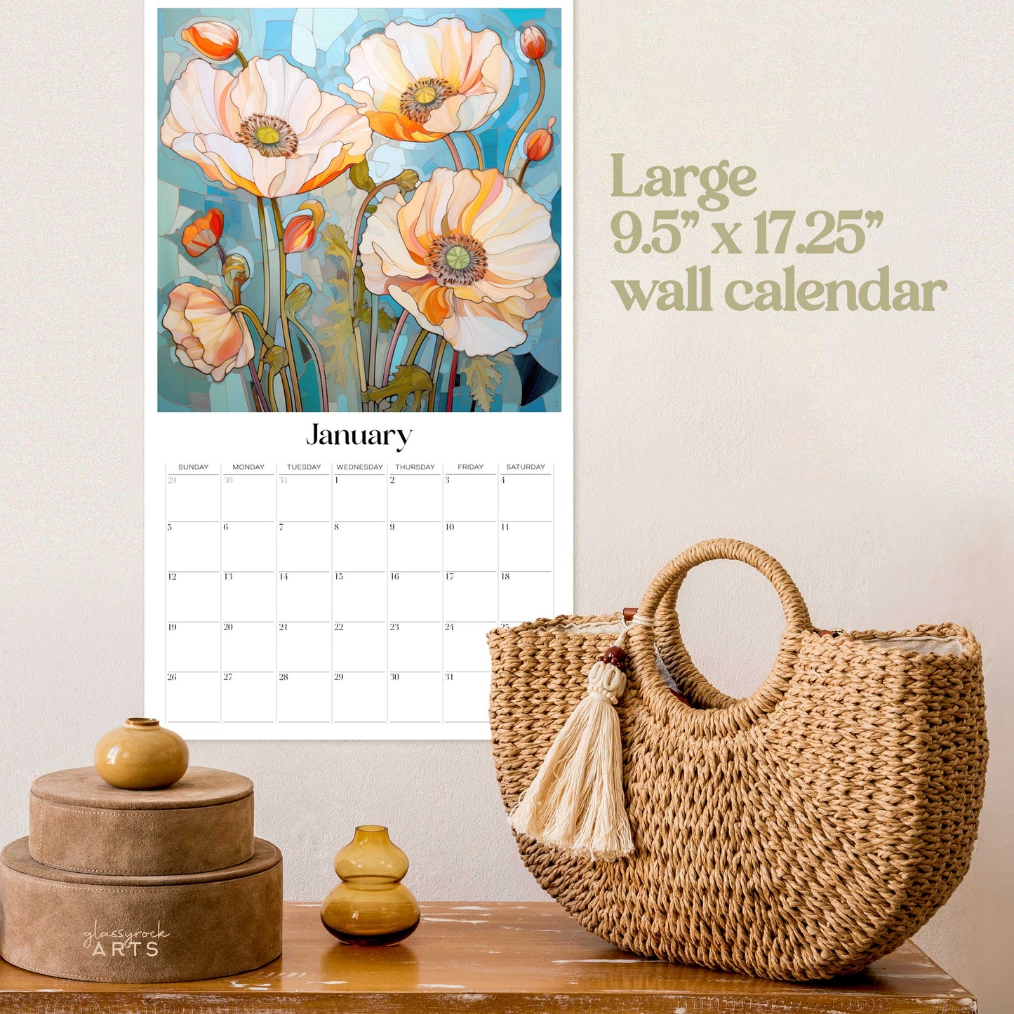 Above, the 2025 Poppies Wall Calendar featuring floral art of orange poppies hangs. Below, a woven basket with a white tassel sits on wood next to small vases and stacked boxes. The text reads, Large 9.5” x 17.25” wall calendar.