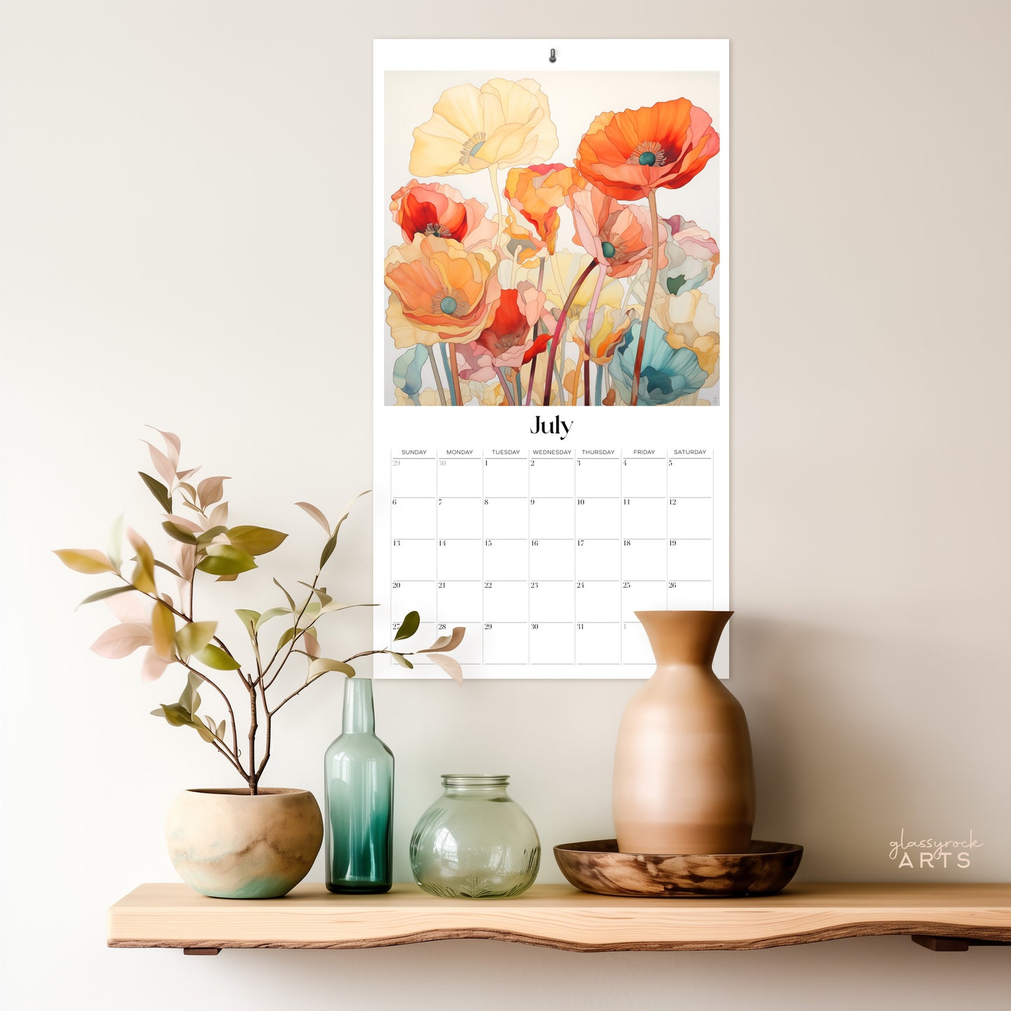 The 2025 Poppies Wall Calendar, featuring vibrant watercolor poppies in a floral theme, hangs above a wooden shelf displaying muted-colored vases and a small plant, creating a calm and artistic atmosphere.