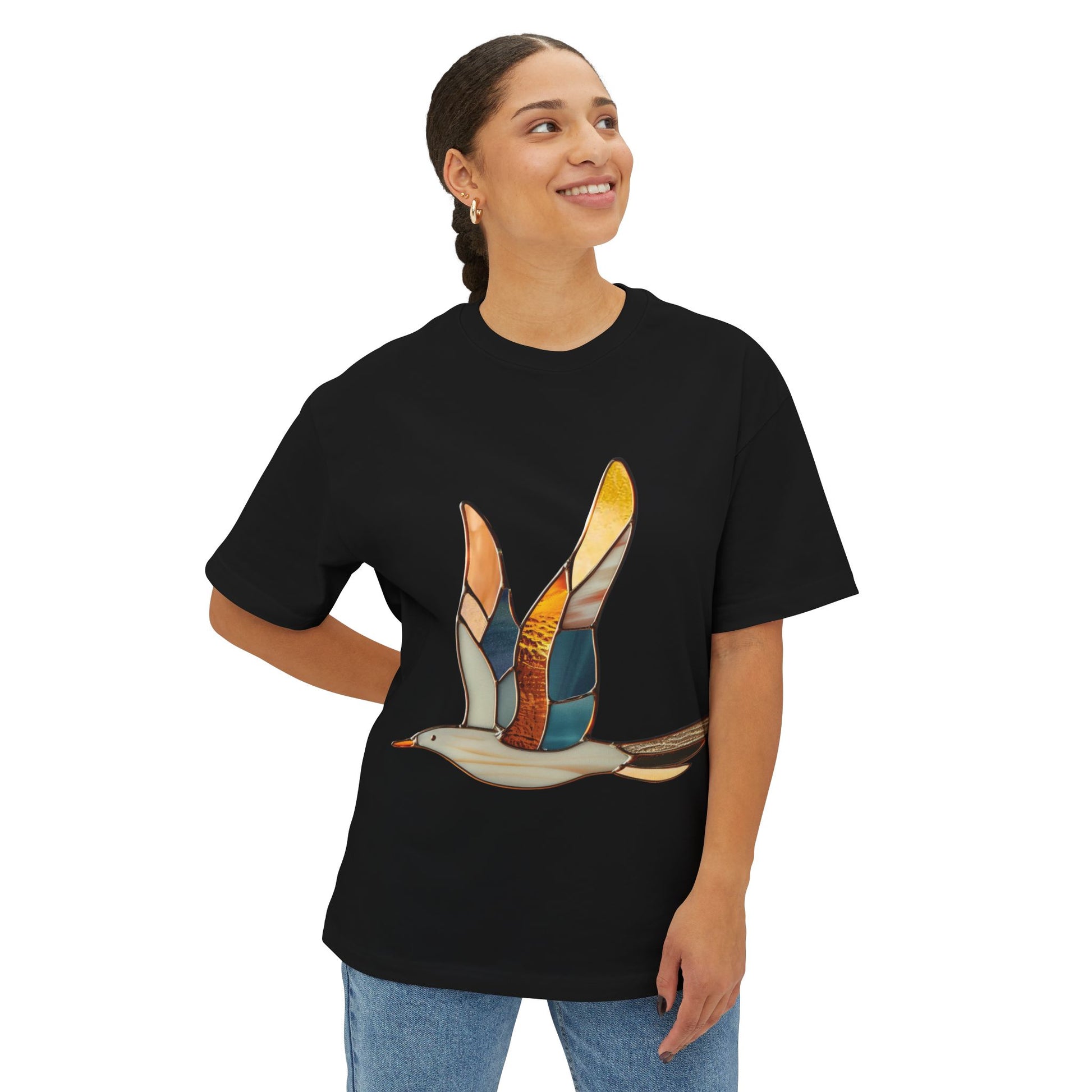 A person wearing an oversized, black Stained Glass Seagull Tee Shirt from Bella+Canvas stands smiling with one hand on their hip.