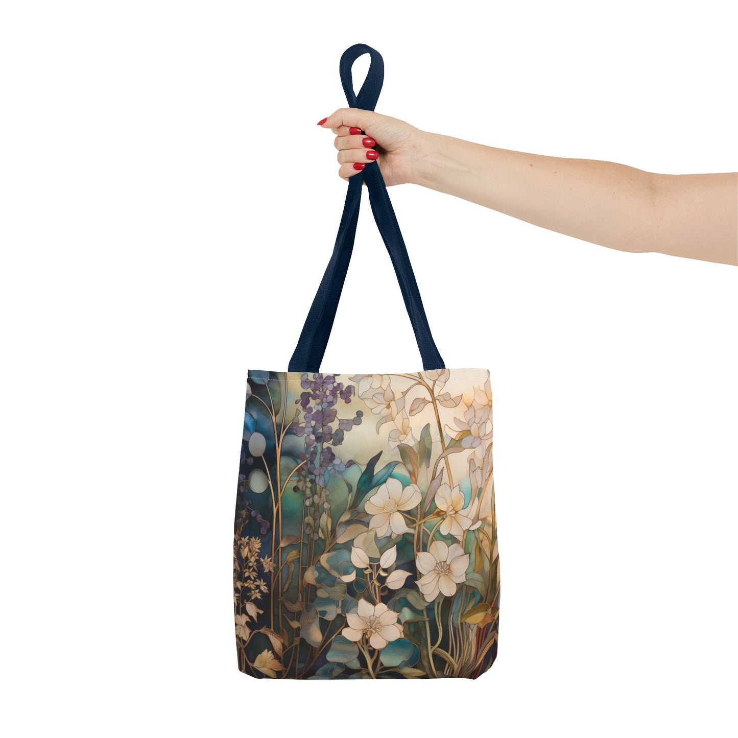 A hand with red-painted nails holds the Stained Glass Midnight Flowers Tote Bag, showcasing a floral design in blue, white, and beige against a muted background. Crafted from durable polyester with dark handles, the bag stands out against the plain white backdrop.