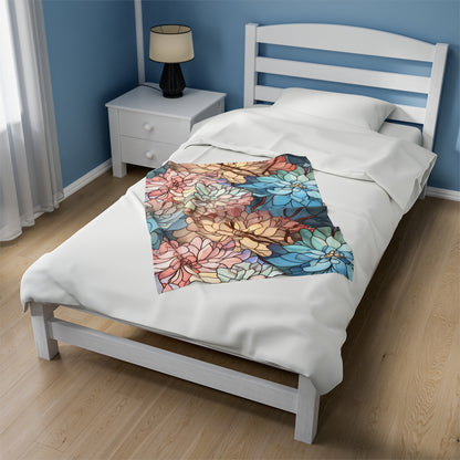 A white bed adorned with a Stained Glass Flowers Soft Plush Blanket, showcasing vibrant red, blue, and yellow flowers. The room is painted blue and features light hardwood flooring, a bedside lamp, and a white curtain partially covering the window.