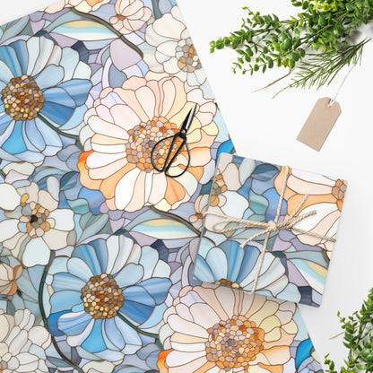 The Stained Glass Flowers Wrapping Paper, adorned with large blue and peach floral patterns, is displayed with scissors and a twine-tied gift. Greenery and a blank tag accent the scene on a white surface, highlighting the elegance of this premium gloss paper.