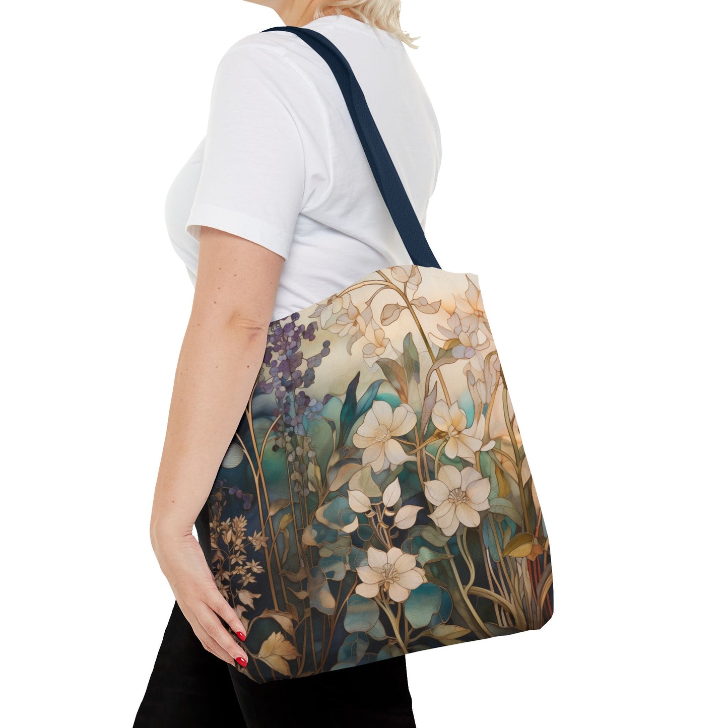 A person in a white t-shirt carries the Stained Glass Midnight Flowers Tote Bag, featuring flowers and leaves in soft, natural colors. Made from durable polyester materials, the black strap provides contrast against the white background.