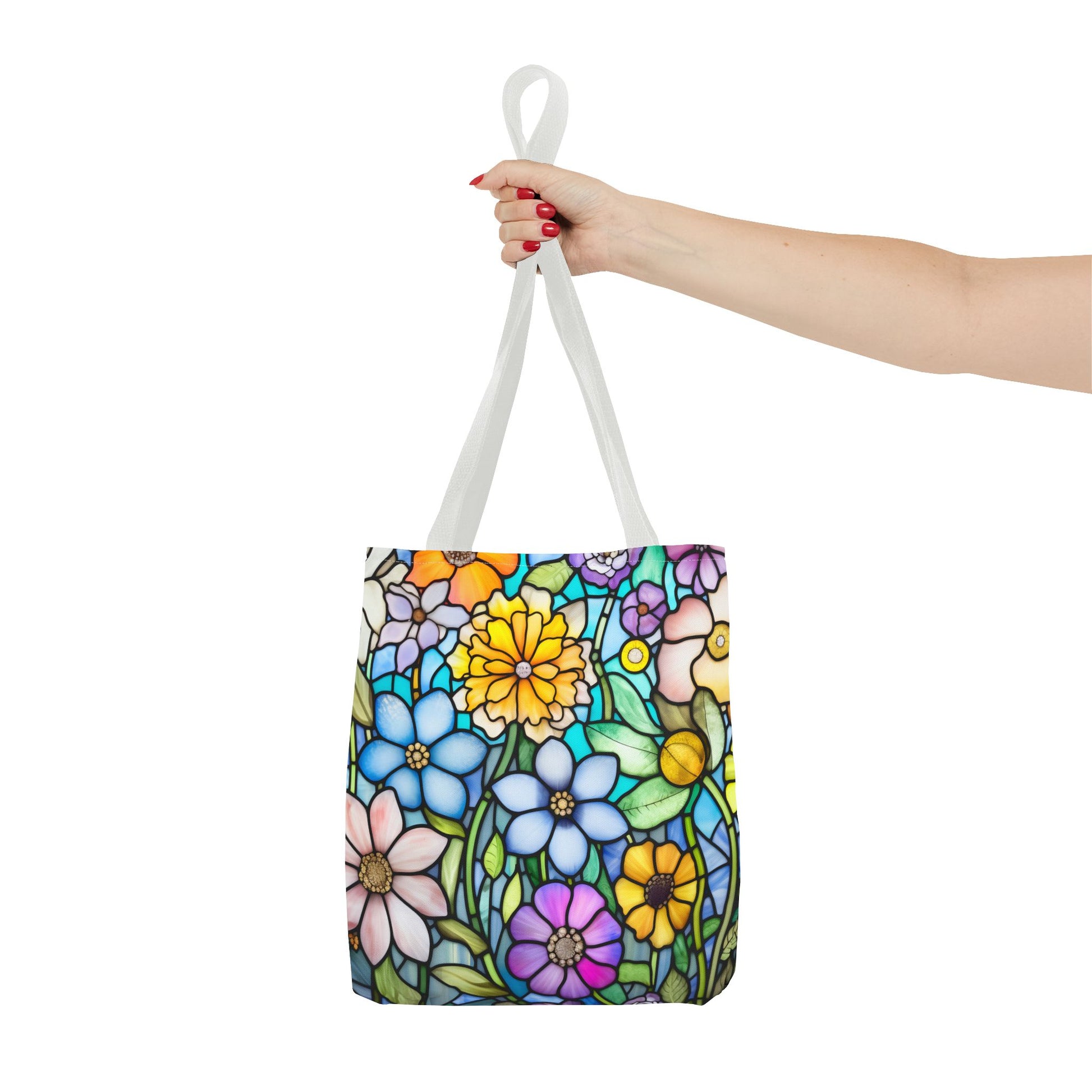 A hand holds the Stained Glass Folk Art Flowers Tote Bag, featuring a vibrant floral design with blue, yellow, purple, and green hues on white. Made from durable polyester with white handles, it combines style and sturdiness.