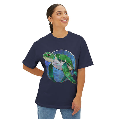 A person dressed in a Stained Glass Turtle Oversized Tee Shirt by Bella+Canvas, featuring a vibrant sea turtle design in navy blue, is smiling and looking upwards.