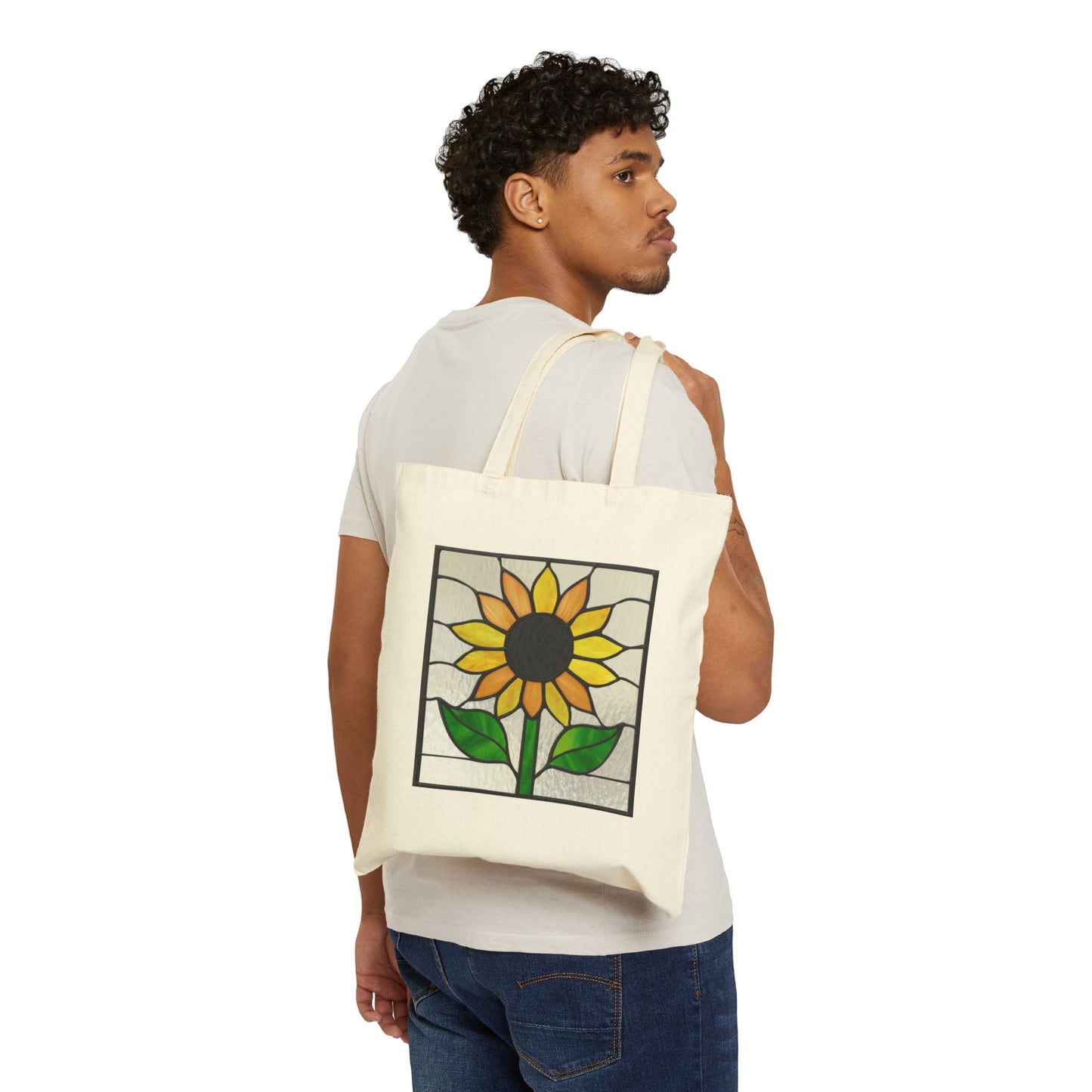 A person with short curly hair, in a white t-shirt and jeans, glances back while carrying the beige Stained Glass Sunflower Cotton Canvas Tote Bag. The simple white backdrop emphasizes the totes vibrant sunflower design.