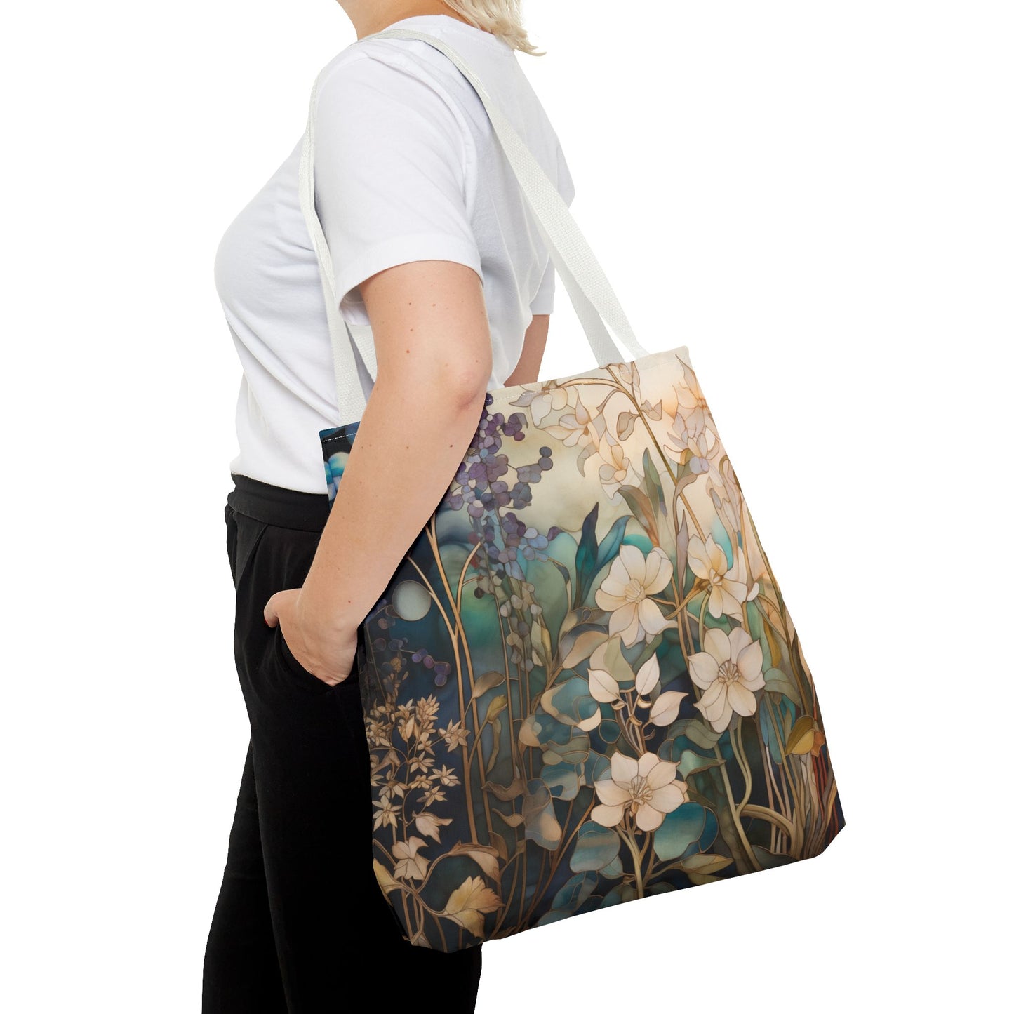 A person, wearing a white shirt and black pants with only their torso shown, carries the Stained Glass Midnight Flowers Tote Bag featuring blue, green, and beige floral patterns on durable polyester.