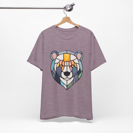 A Bella+Canvas Stained Glass Patchwork Bear Unisex Tee Shirt, featuring a colorful graphic of a bear face depicted in stained glass art, hanging on a wooden hanger suspended from a metal rod.