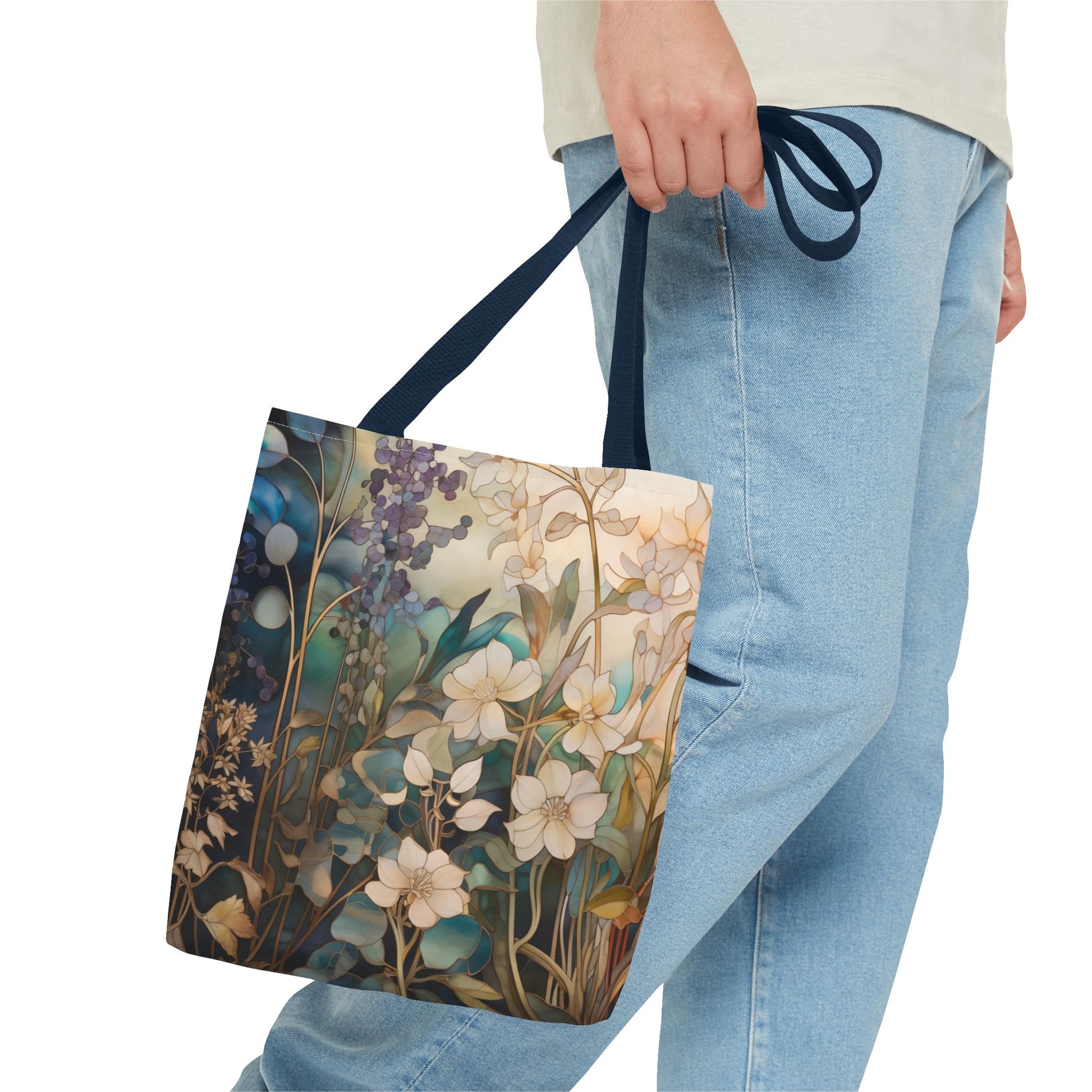 A person in light blue jeans and a light shirt holds a Stained Glass Midnight Flowers Tote Bag, featuring white floral designs with green leaves on a durable polyester navy strap.