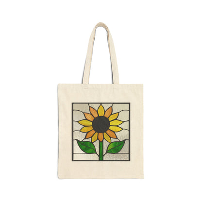 A beige cotton canvas tote bag features a unique stained glass sunflower design with yellow petals, a dark center, and green leaves against a light textured background.