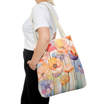 Person holding a Stained Glass Poppy Flowers Tote Bag, available in 3 sizes, crafted from durable polyester. The tote bag features vibrant shades of orange, red, yellow, and purple flowers in a stunning floral design. The person is wearing a white t-shirt and black pants.