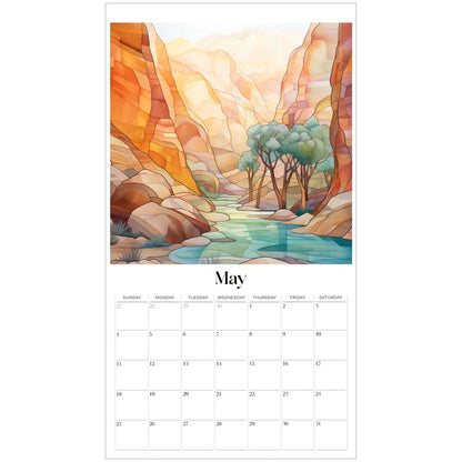 The May page of the 2025 Desert Landscapes Large Wall Calendar displays a watercolor of a serene canyon, resembling stained glass, with vibrant orange and yellow cliffs, a calm river, and trees. Dates are arranged in a grid beneath the illustration.