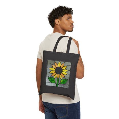 A curly-haired person in a white t-shirt and blue jeans carries the Stained Glass Sunflower Cotton Canvas Tote Bag, featuring a chic stained glass-style sunflower design with vibrant green leaves.