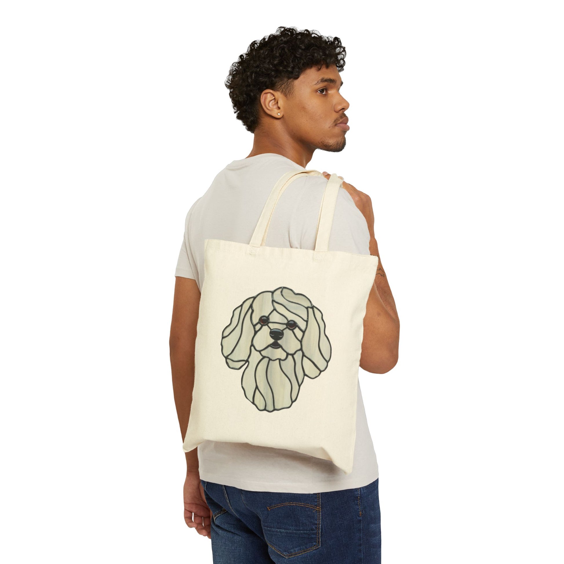 A man in a white t-shirt and blue jeans carries a Stained Glass Bichon Frise Cotton Canvas Tote Bag.