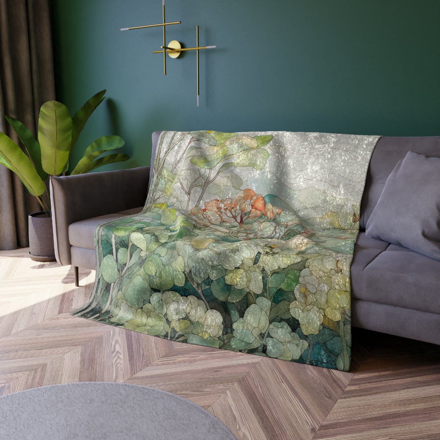 A sofa with a Stained Glass Tropical Forest Crushed Velvet and Soft Fleece Blanket - 50x60 draped over it sits against a green wall. A potted plant is on the left, and a modern circular wall light is above. The floor features a wooden herringbone pattern.