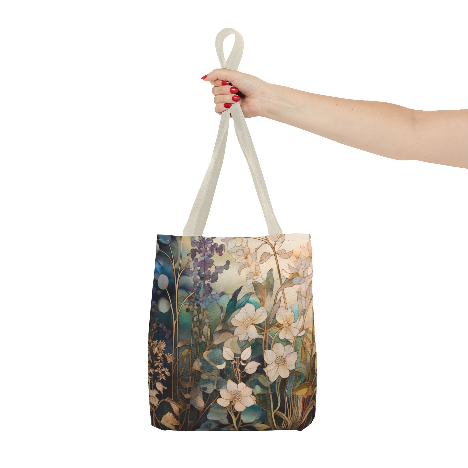 A hand with red nail polish holds the Stained Glass Midnight Flowers Tote Bag, featuring a floral design with white and purple flowers on a green and brown backdrop. Made from durable polyester, it is finished with light-colored handles.