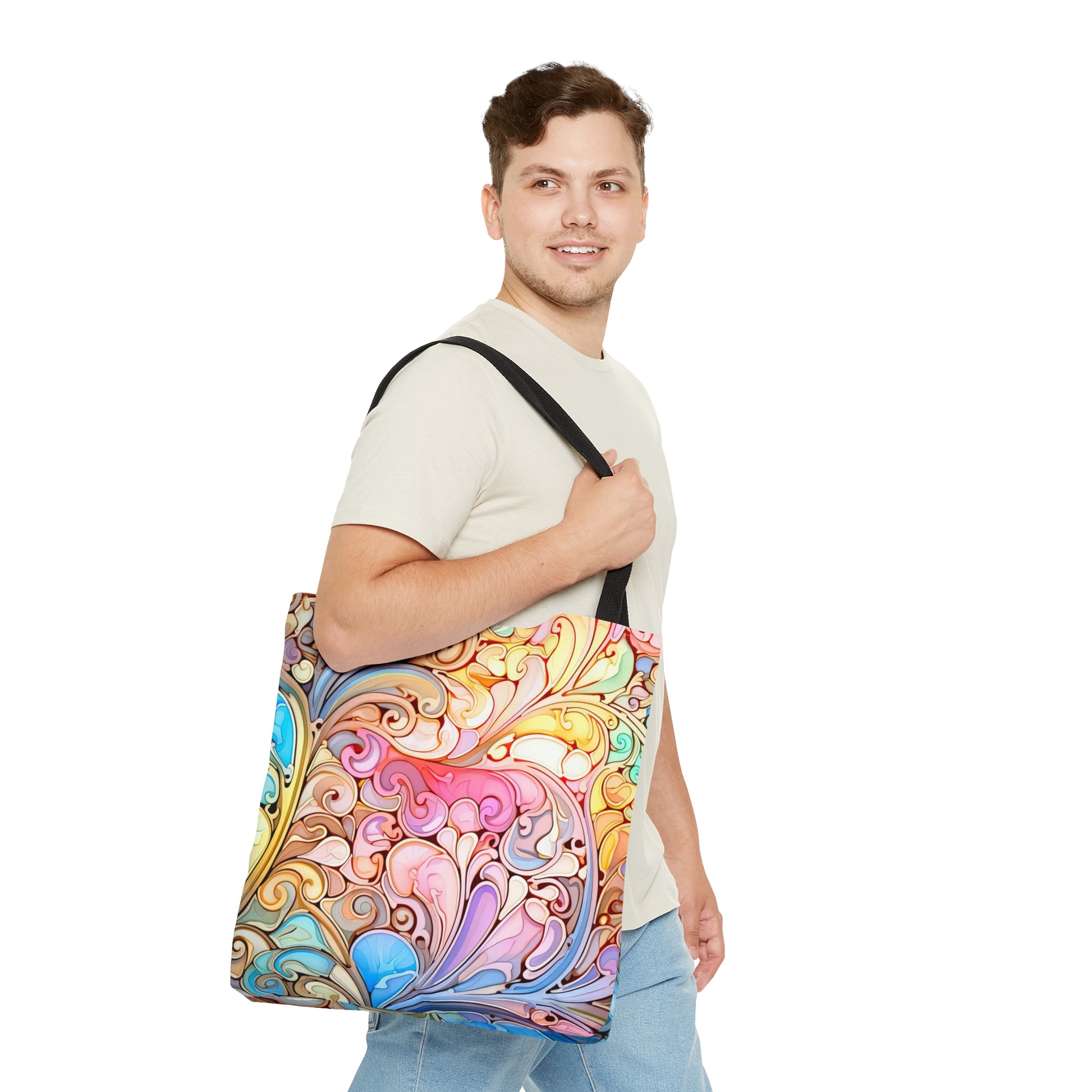 A person with light brown hair and a short beard is smiling while holding the Rainbow Paisley Stained Glass Tote Bag, an ideal boho gift, featuring an intricate and vibrant swirling pattern reminiscent of stained glass, over their shoulder.