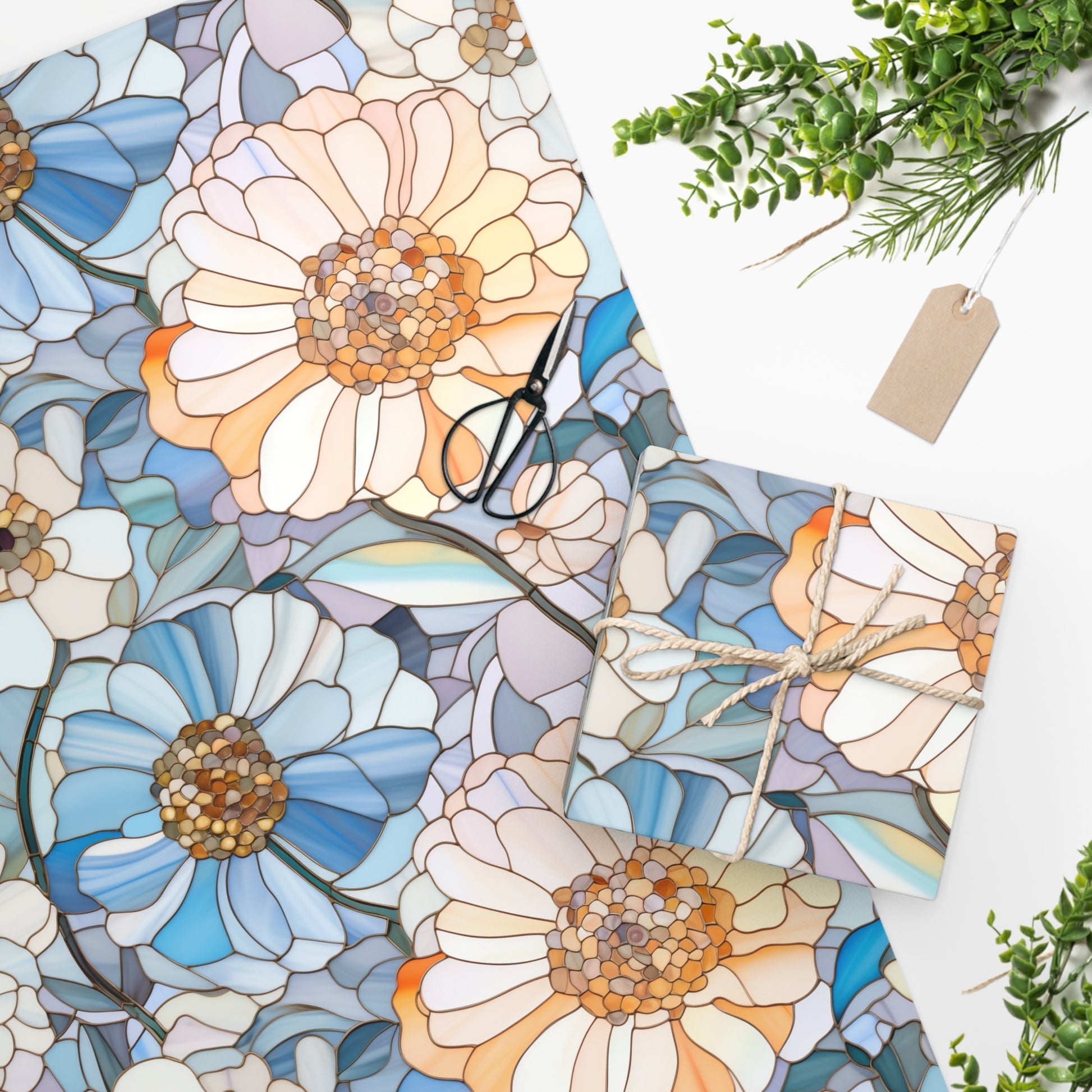 The Stained Glass Flowers Wrapping Paper showcases blue and peach floral designs, paired with a gift wrapped in premium gloss paper and natural twine. Scissors, a blank tag, and green foliage are elegantly arranged on a white surface.