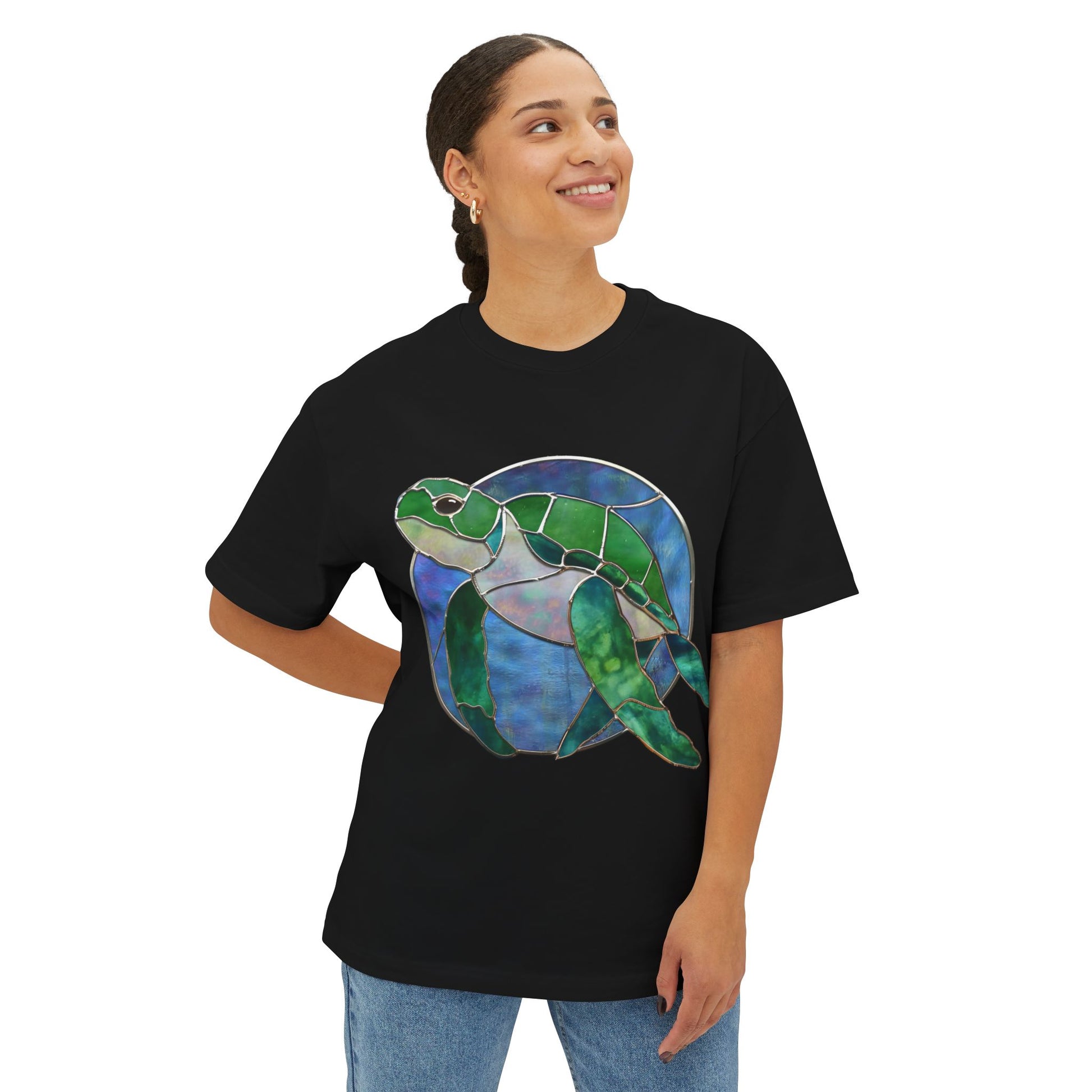 Person standing, smiling, wearing a black Stained Glass Turtle Oversized Tee Shirt with a graphic design of a stained-glass style sea turtle by Noelle Barnes.