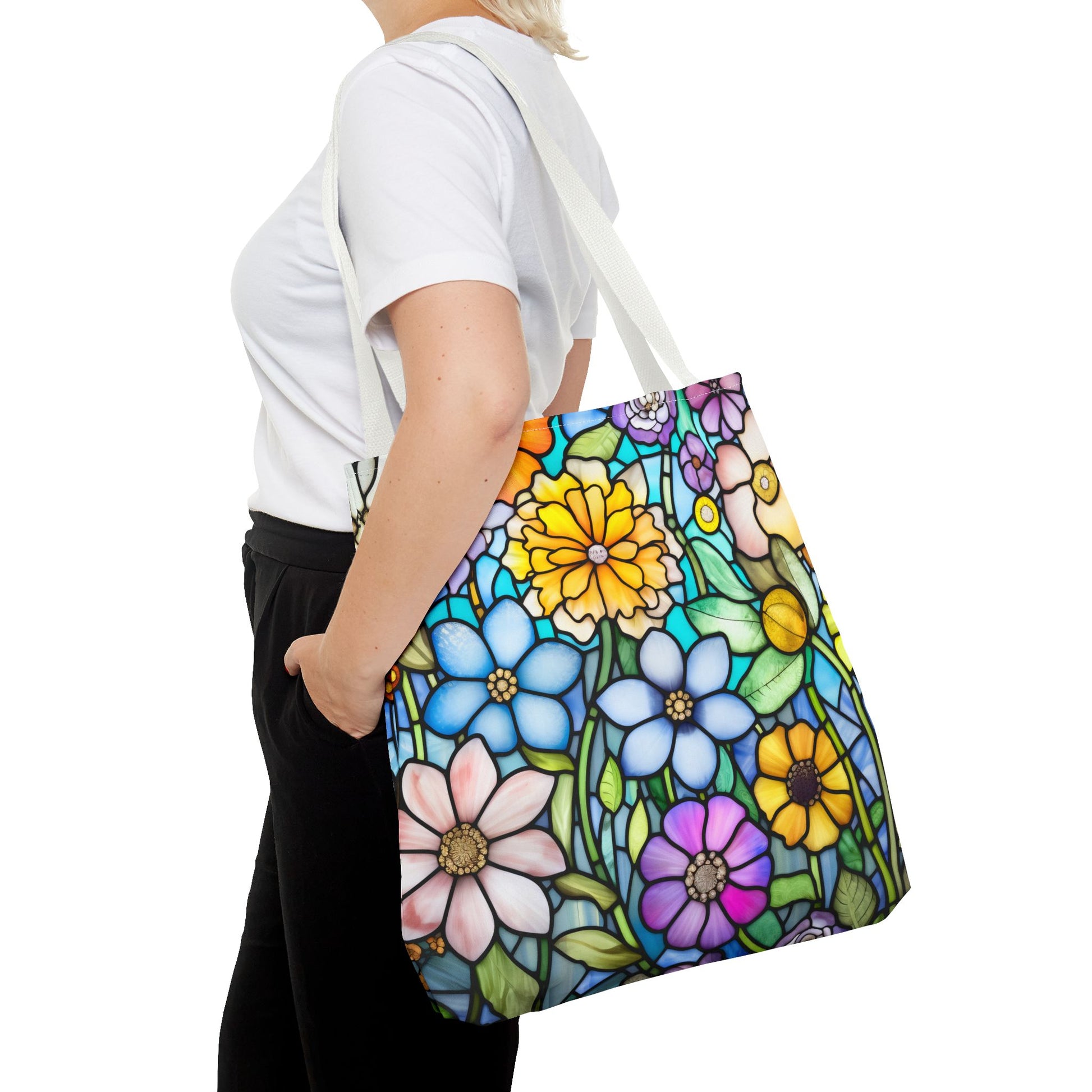 A person carries the Stained Glass Folk Art Flowers Tote Bag—featuring an original design of colorful daisies and sunflowers on white, made from durable polyester—which perfectly complements their white shirt and black pants.