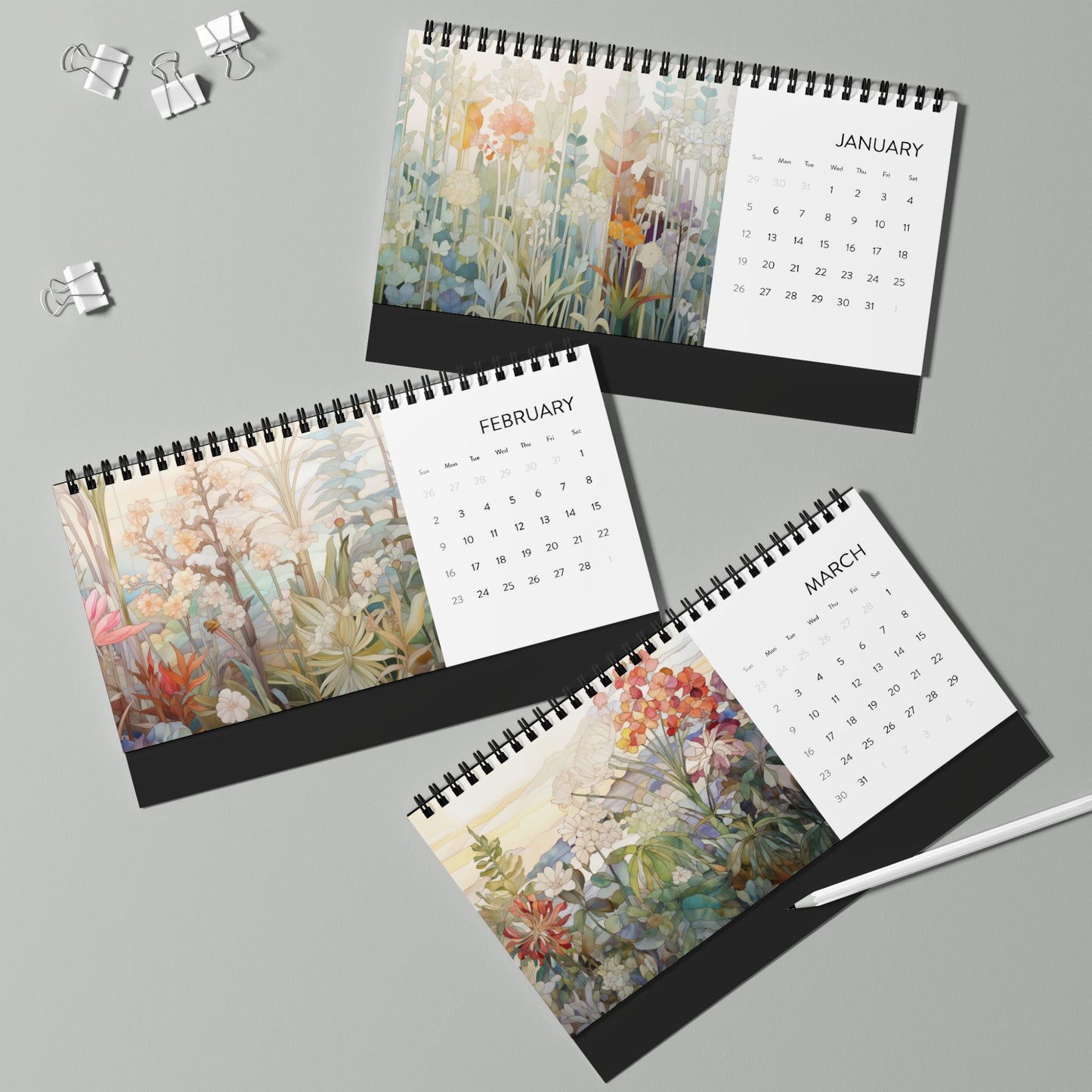 The 2025 Desk Calendar - Botanicals, featuring the months of January, February, and March with beautiful floral illustrations on high-quality paper stock, along with a pen and paper clips, displayed on a light green surface.