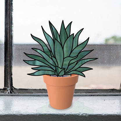 A pack of four Stained Glass Succulent Stems with long, pointed leaves sits in a terra cotta pot on the windowsill, adding warmth, while an illustrated effect enhances the blurred outdoor view through the window.