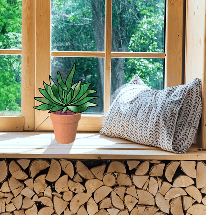 A stained glass window accentuates the green leaves of a potted succulent on the sill, next to a patterned pillow. Sunlight filters in, highlighting piled firewood while trees sway outside. Featured: Stained Glass Succulent Stems Pattern Pack of 4.