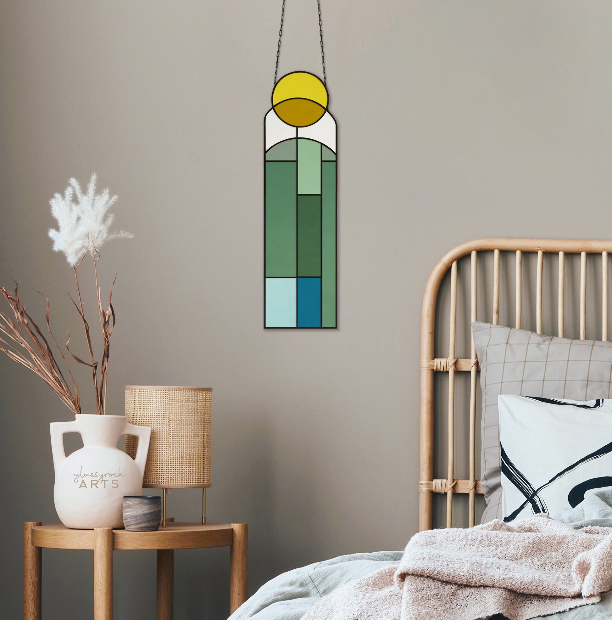 A cozy bedroom in neutral tones features a wooden bed with pillows, a plant in a white pot, and a woven lamp on the nightstand. The wall is adorned with an Abstract Sunset Stained Glass Pattern, showcasing digital geometric designs in shades of green, blue, and yellow.