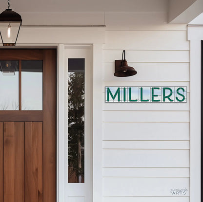 The front porch features a wooden door and sidelight window. A white wall displays a teal and white MILLERS sign. Above it, a black sconce lamp evokes the style of the Stained Glass Alphabet Pattern Pack, while a hanging lantern completes the entrance.