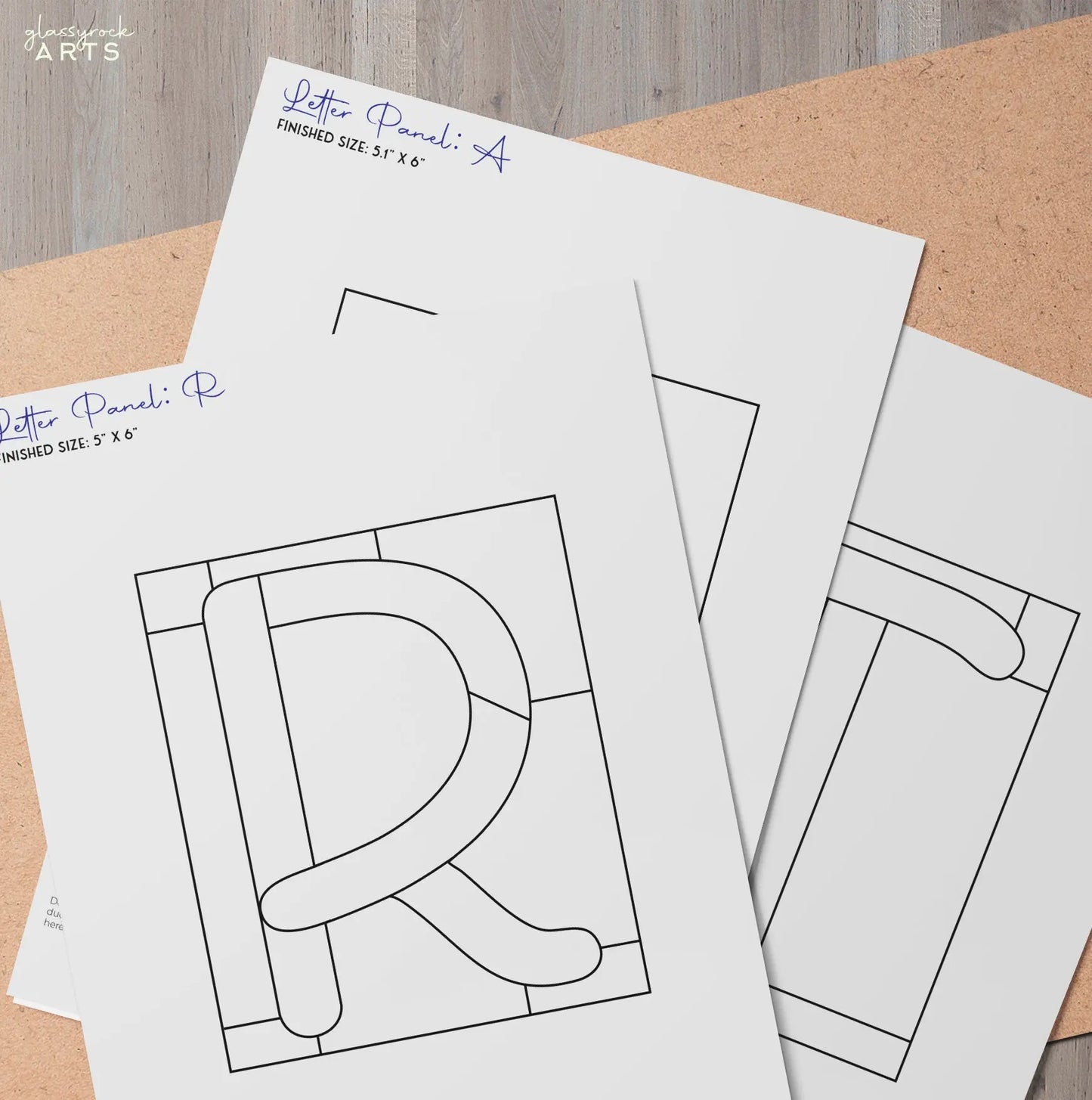 Three sheets on a wooden surface display geometric letter designs like R and P, with bold lines in squares, from the Stained Glass Alphabet Pattern Pack, meticulously labeled with dimensions and signatures.