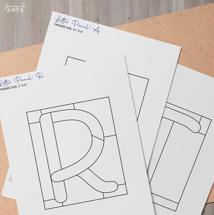 Three sheets on a wooden surface display geometric letter designs like R and P, with bold lines in squares, from the Stained Glass Alphabet Pattern Pack, meticulously labeled with dimensions and signatures.