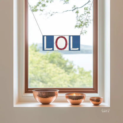 A window displays a blue and red sign LOL. Below, three copper bowls of various sizes rest on the windowsill, their reflections shining like those from the Stained Glass Alphabet Pattern Pack. In the background, trees and a hint of water can be seen.