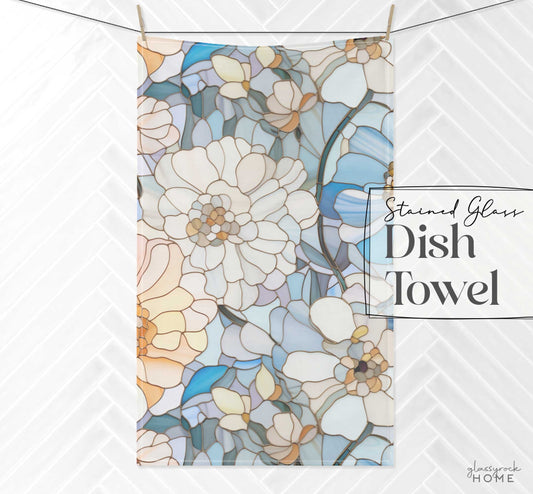 A dish towel with a stained glass floral pattern of white, blue, and peach flowers is set against a white background. The text reads Stained Glass Flowers Kitchen Towel in elegant script—ideal as a boho gift to elevate your kitchen decor.