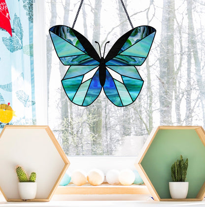 The Beginner Butterfly Stained Glass Pattern adorns the window with its blue and green hues, while snow-covered trees stand tall outside. Inside, hexagonal shelves hold small potted cacti and plants, forming a cozy indoor oasis amidst the winter scenery.