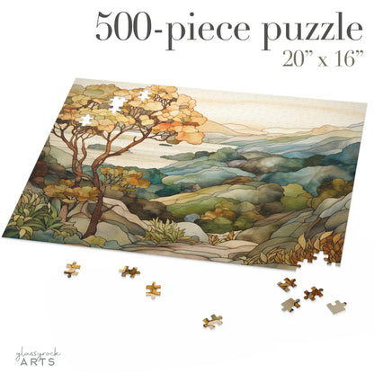 A jigsaw puzzle with a coastal scene of the Big Sur area of California, with a large tree on the left and mountains on the right and ocean in the distance. The illustration is in a stained glass style in muted colors.  500 pieces.