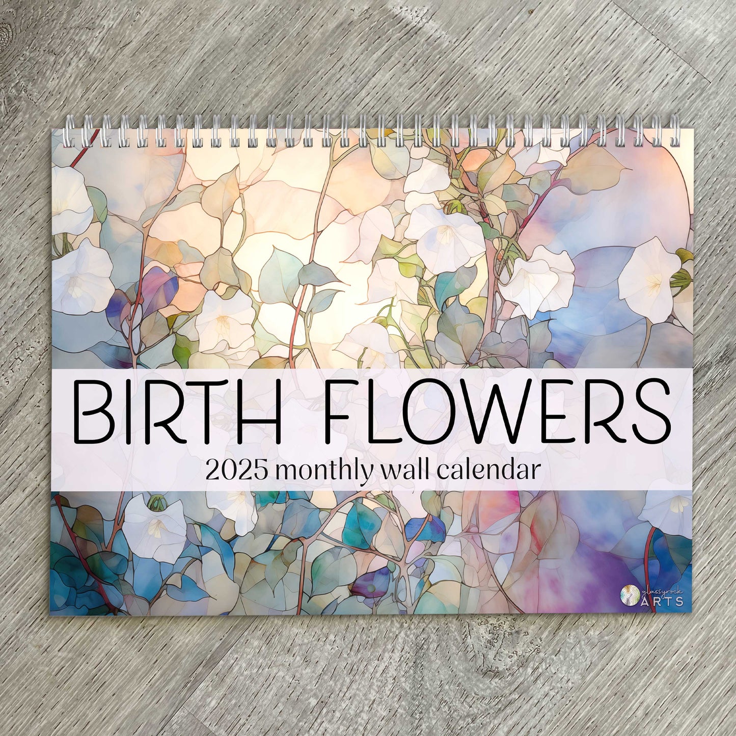 The birth flowers calendar, a 2025 monthly wall calendar with flower-themed original artwork, on a wood table surface. 