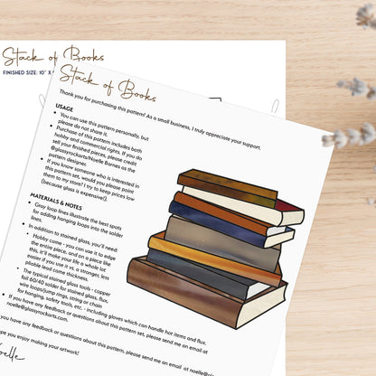 The Books Stained Glass Pattern showcases a stack of books with an overlay of usage instructions and material details, ideal as a gift for book lovers. Handwritten notes and decorative text appear on a light wooden surface with a small plant nearby.