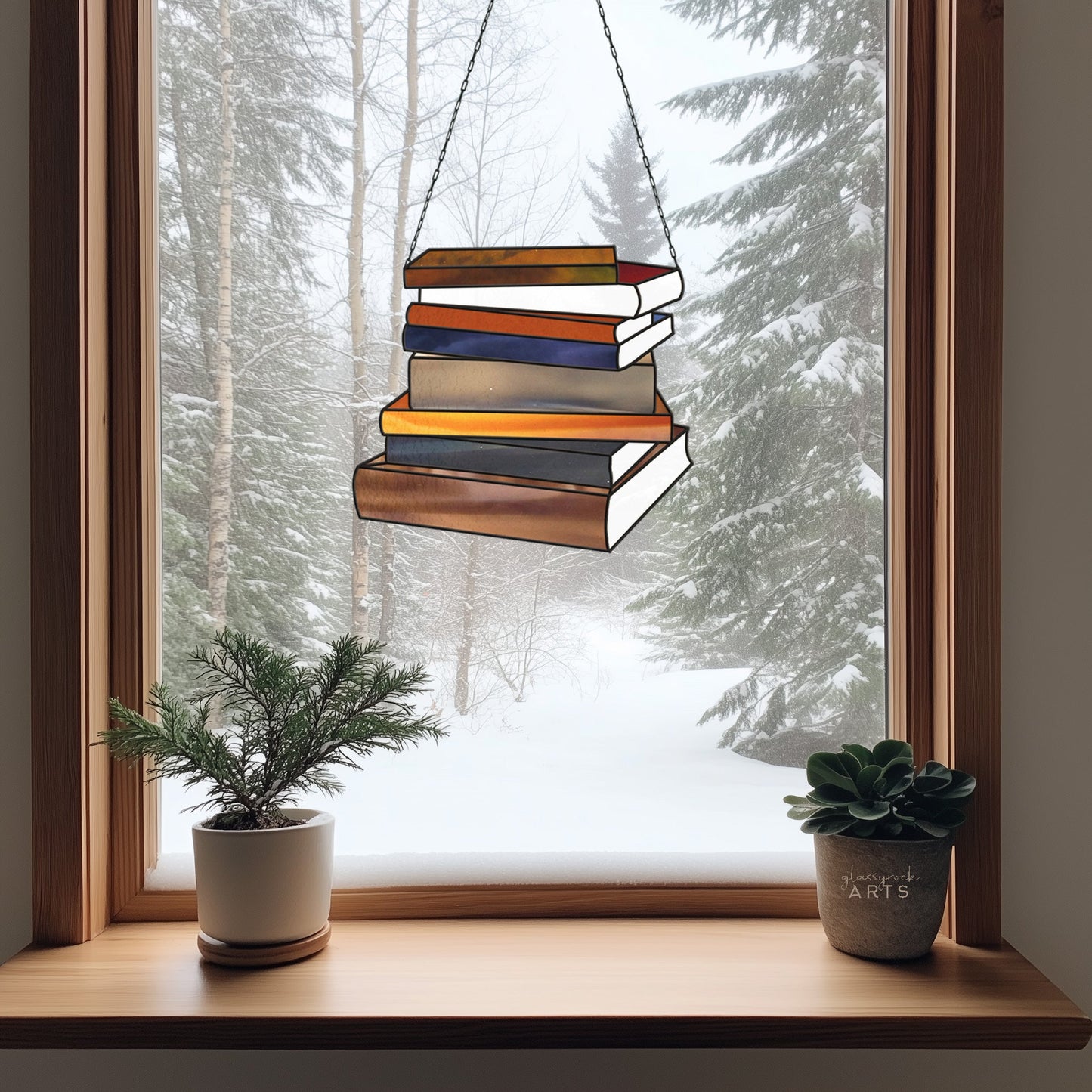 A window reveals a snowy forest scene and a Books Stained Glass Pattern ornament, ideal as a librarian gift. Below, an evergreen plant and succulent enhance the wooden windowsills charm.