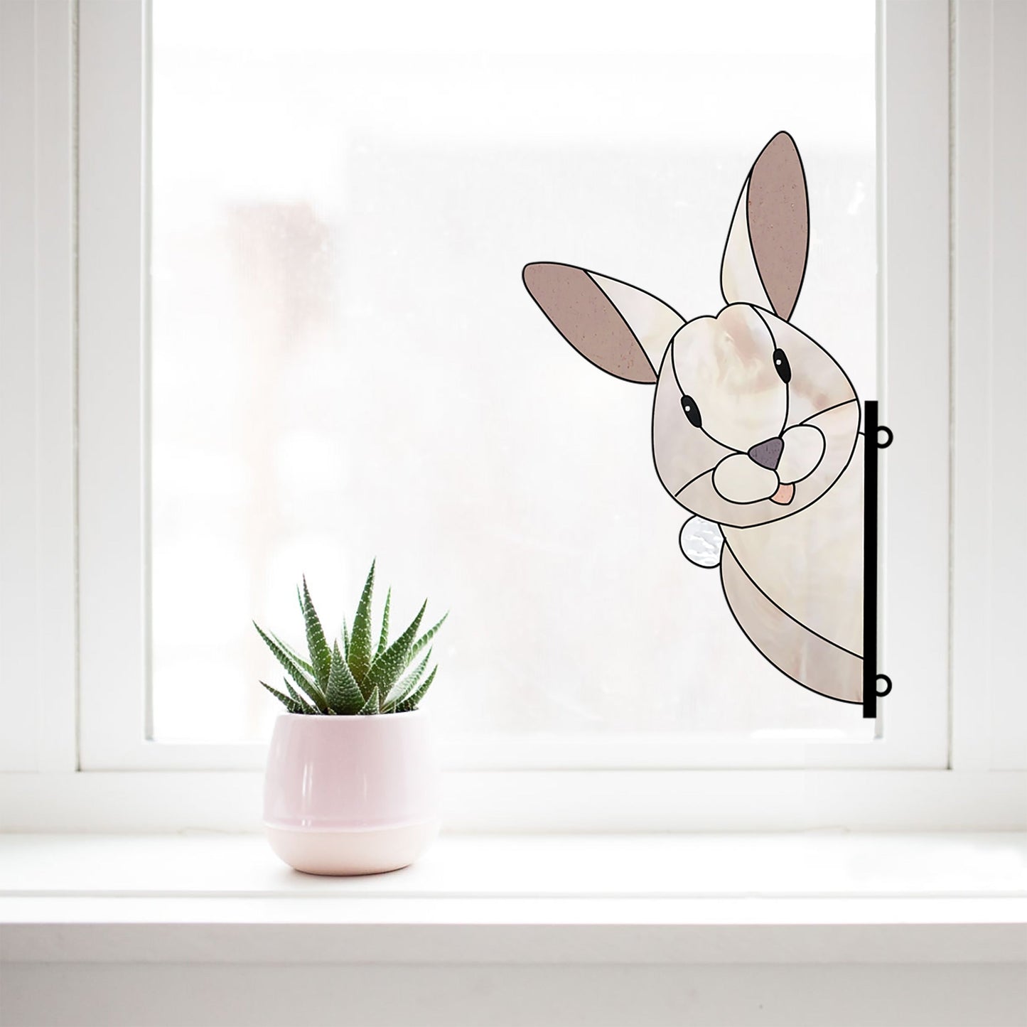 The Rabbit Buddy Bunny stained glass rabbit pattern decorates the window, available for digital download with a commercial license. Beside it sits a small green succulent in a light pink pot on the white windowsill.