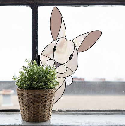 A woven basket holds a potted plant on the windowsill. Outside, a cartoon bunny inspired by the vibrant Rabbit Buddy Bunny Stained Glass Rabbit Pattern peeks over the edge. The blurred rooftops and sky in the background create an enchanting scene.