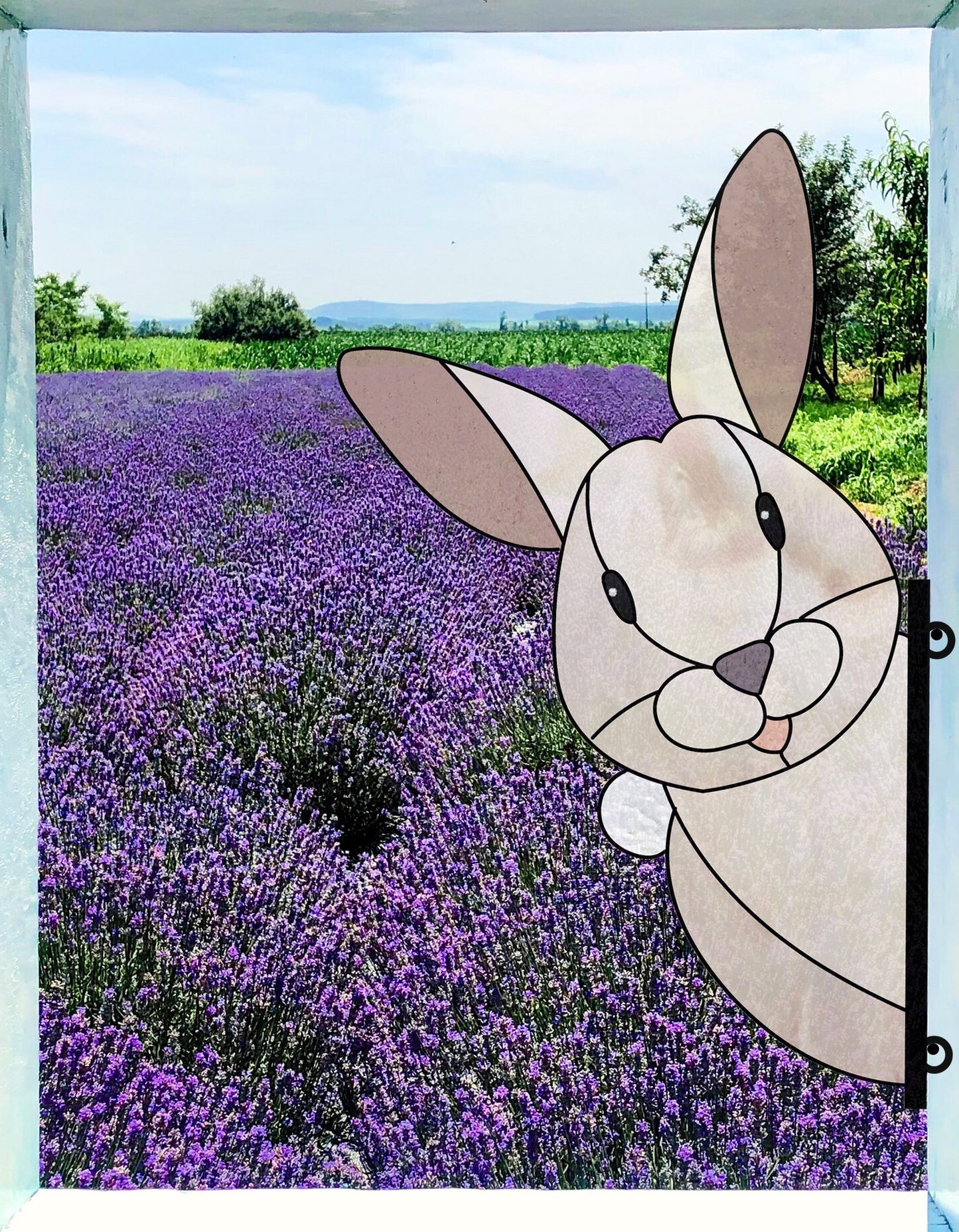 A scenic lavender field under a clear blue sky showcases vibrant purple flowers. A cartoon bunny, inspired by the Rabbit Buddy Bunny Stained Glass Pattern, playfully peeks in from the side, adding a whimsical touch to the serene landscape.